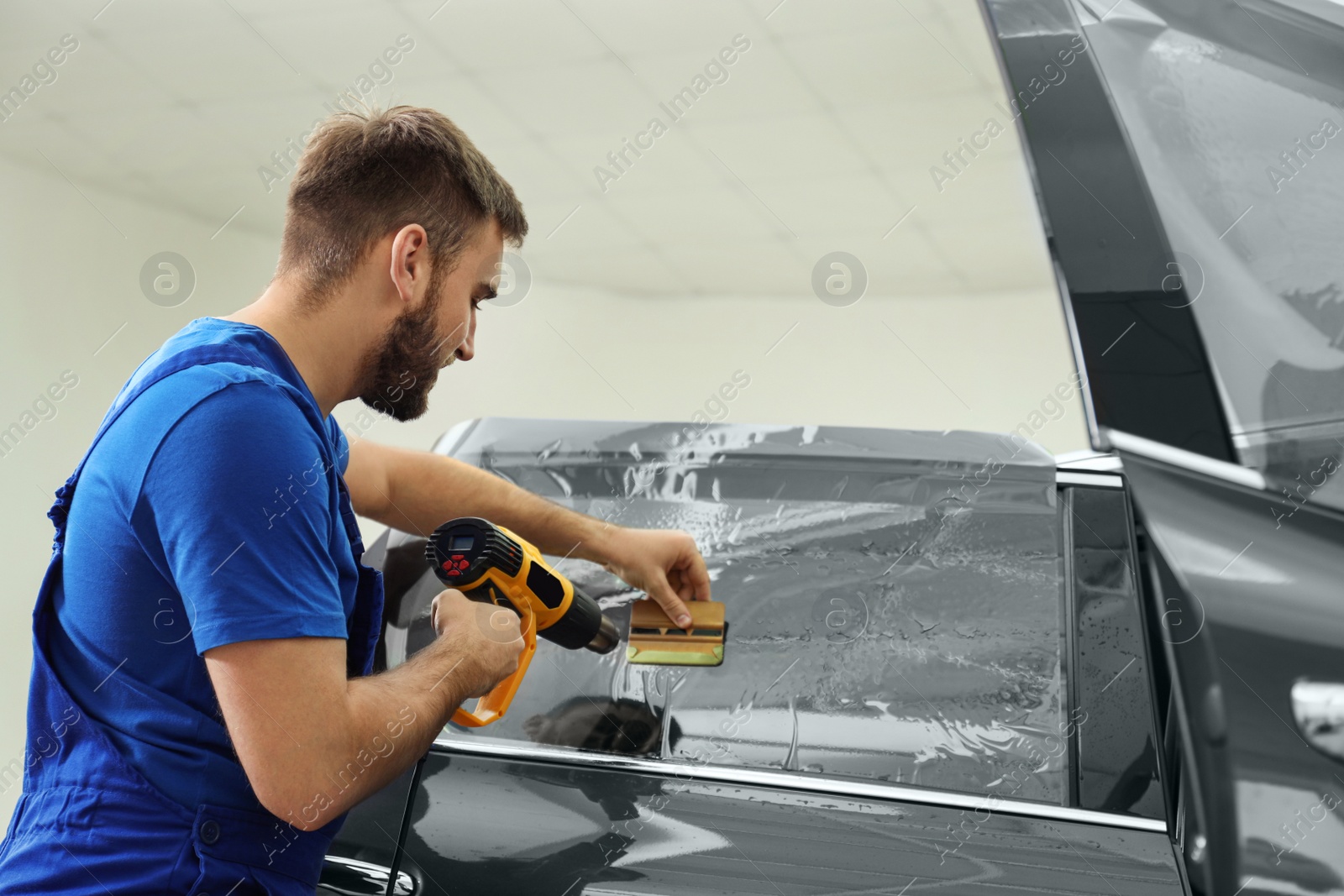 Photo of Worker tinting car window with heat gun in workshop