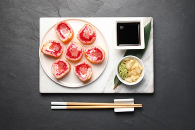 Delicious sushi rolls and chopsticks on black textured table, flat lay