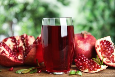 Photo of Pomegranate juice in glass and fresh fruits on wooden table outdoors