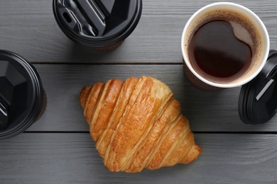 Photo of Coffee to go. Paper cups with tasty drink and croissant on grey wooden table, flat lay