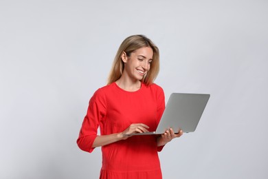 Portrait of young woman with modern laptop on light grey background