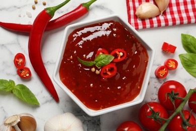 Photo of Spicy chili sauce and ingredients on white marble table, flat lay