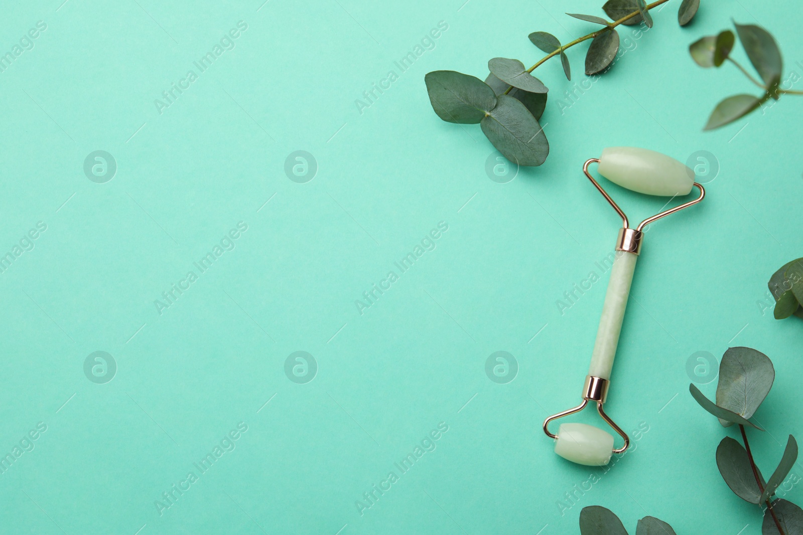 Photo of Natural face roller and eucalyptus on turquoise background, flat lay. Space for text