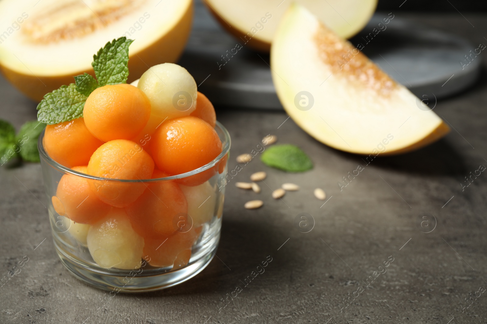 Photo of Melon balls and mint in glass on grey table, closeup. Space for text