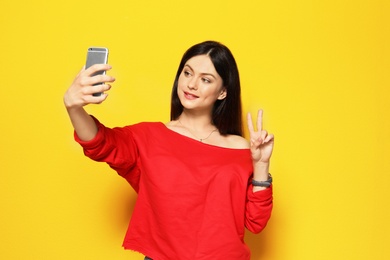 Attractive young woman taking selfie on color background