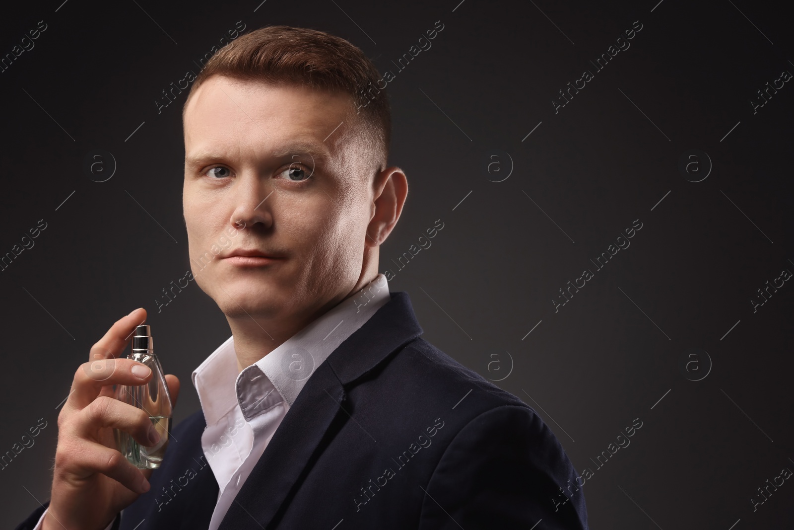 Photo of Handsome man in suit using perfume on dark background