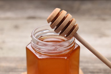 Photo of Sweet honey in jar and dipper on table, closeup