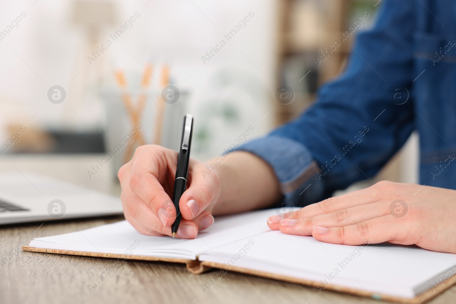 Photo of Young woman writing in notebook at wooden table, closeup