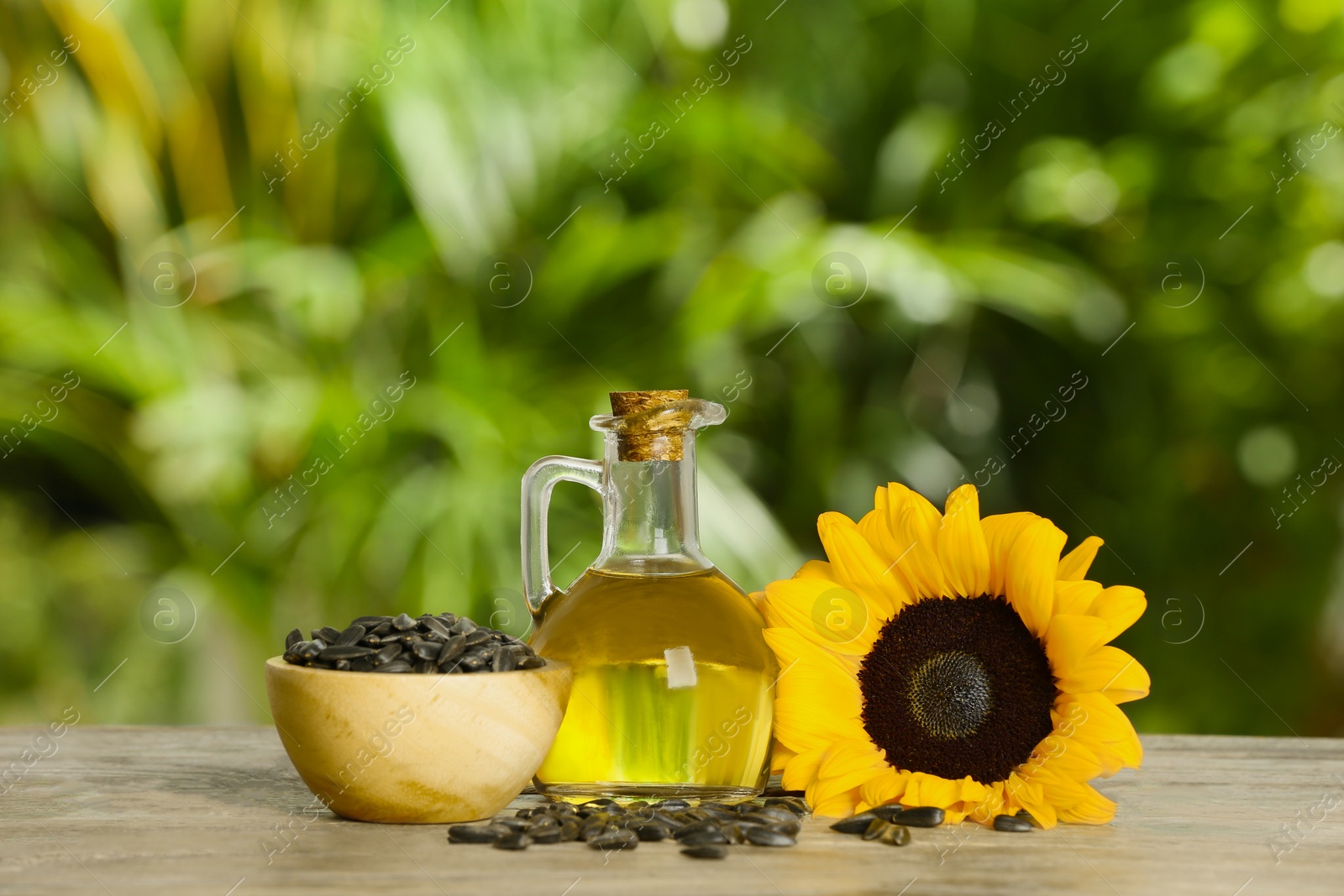 Photo of Sunflower cooking oil, seeds and yellow flower on wooden table outdoors