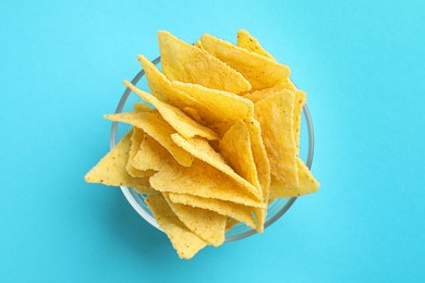 Tortilla chips (nachos) in glass bowl on light blue background, top view