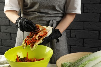 Photo of Woman preparing spicy cabbage kimchi at wooden table indoors, closeup