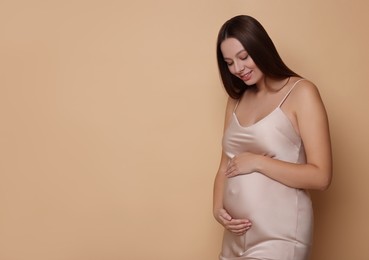 Photo of Beautiful pregnant woman in dress on beige background, space for text
