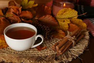 Cup of hot tea, pine cone, cinnamon sticks and autumn leaves on wooden table. Space for text