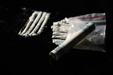 Photo of Drug addiction. Plastic bag with cocaine and rolled dollar banknote on black table, closeup