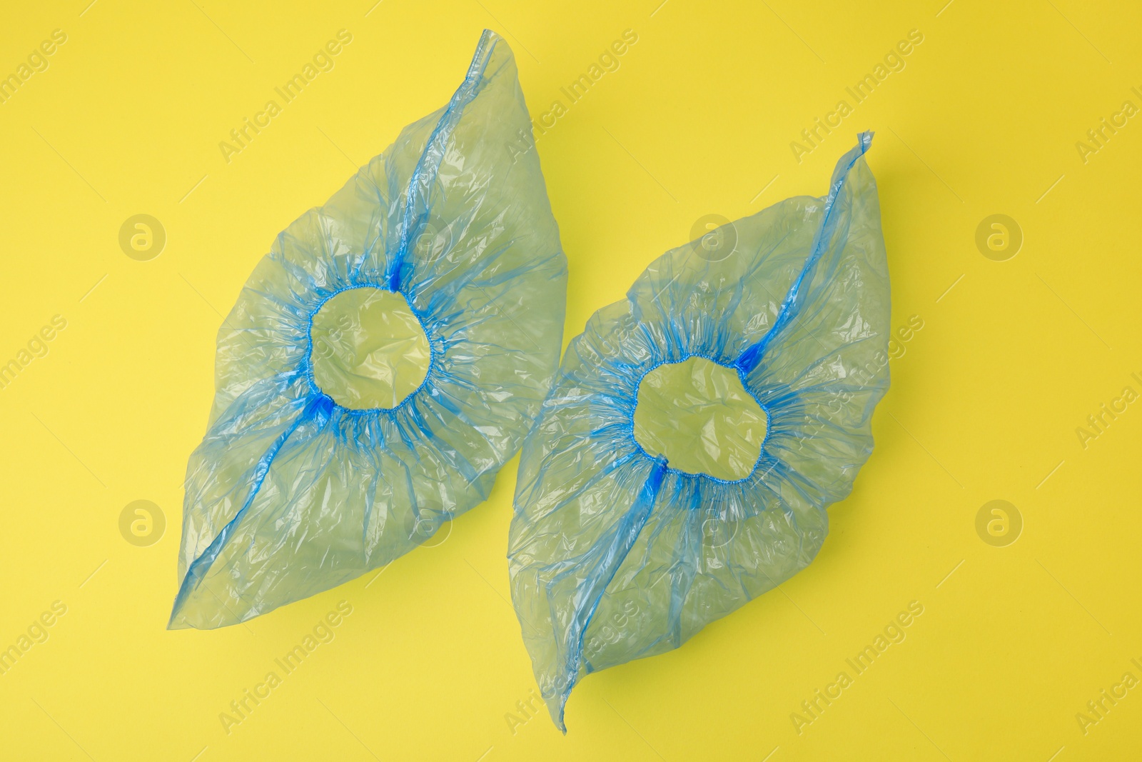 Photo of Pair of blue medical shoe covers on yellow background, top view