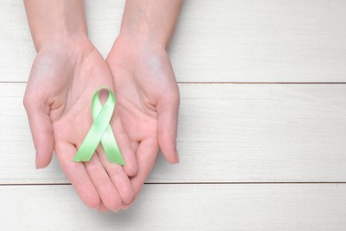 World Mental Health Day. Woman holding green ribbon on white wooden background, top view with space for text