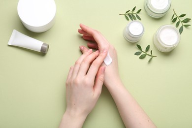 Photo of Woman applying hand cream on green background, top view