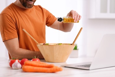 Photo of Man making dinner while watching online cooking course via laptop in kitchen, closeup