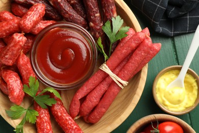 Photo of Different thin dry smoked sausages, parsley and sauces on green wooden table, flat lay
