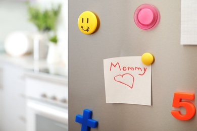 Photo of Note with word "Mommy" and colorful magnets on refrigerator door in kitchen. Space for text