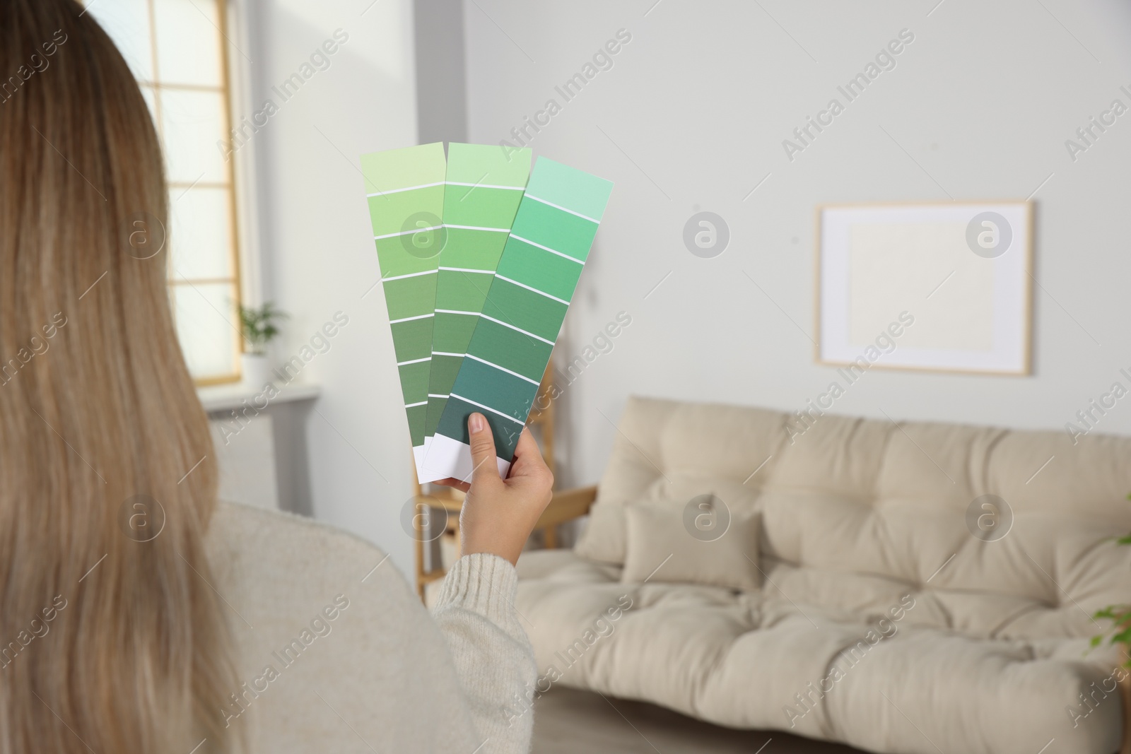 Photo of Woman choosing color for wall in room, focus on hand with paint chips. Interior design