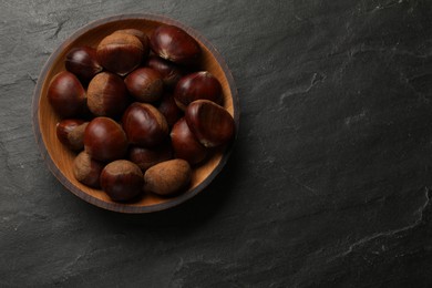 Roasted edible sweet chestnuts in bowl on grey textured table, top view. Space for text