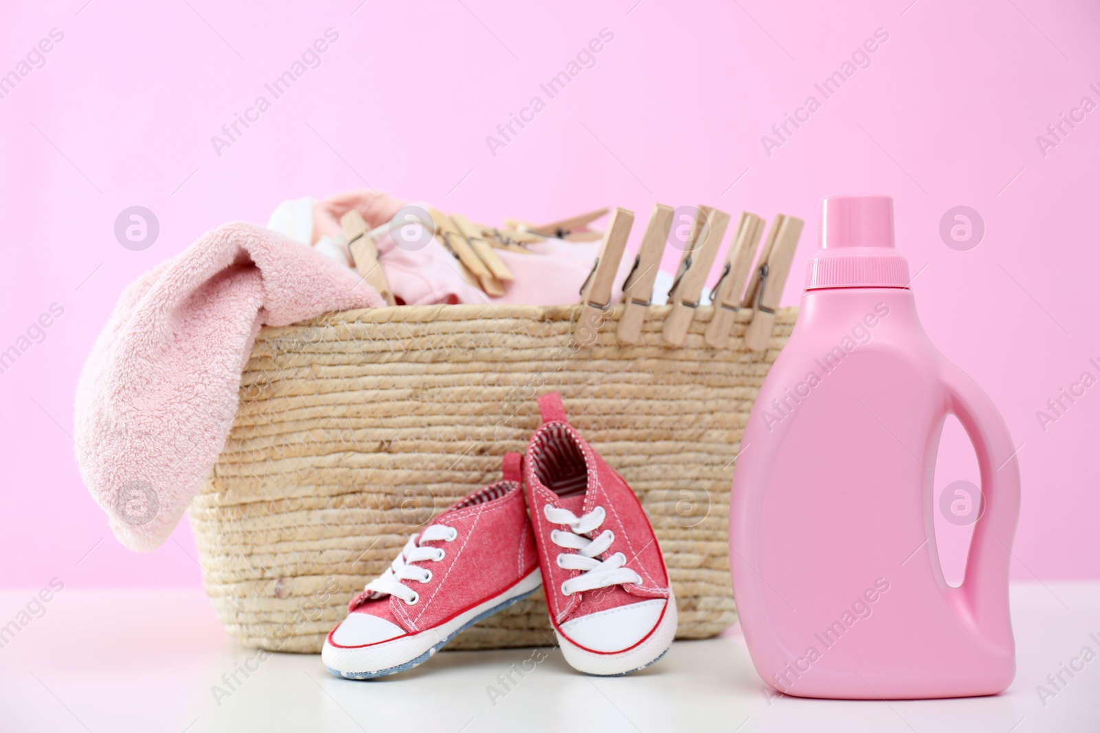 Photo of Detergent and children's clothes on white table