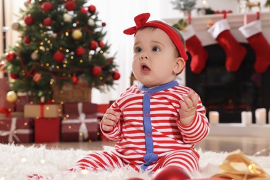 Baby wearing bright Christmas pajamas on floor in room