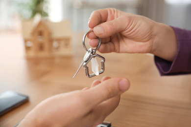 Photo of Real estate agent giving key with trinket to client in office, closeup