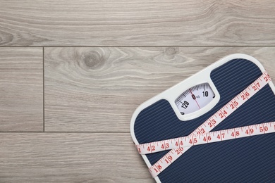 Photo of Scales and measuring tape on wooden background, top view with space for text. Weight loss