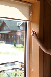 Young woman opening roller curtains at home, closeup