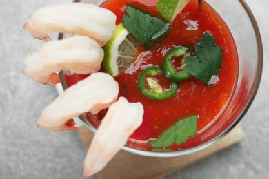 Photo of Tasty shrimp cocktail with sauce, parsley and lime in glass on light grey table, top view