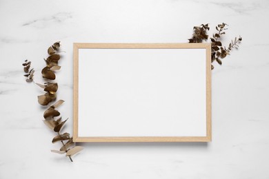 Photo of Empty photo frame and golden dried decorative plants on white marble background, flat lay. Space for design