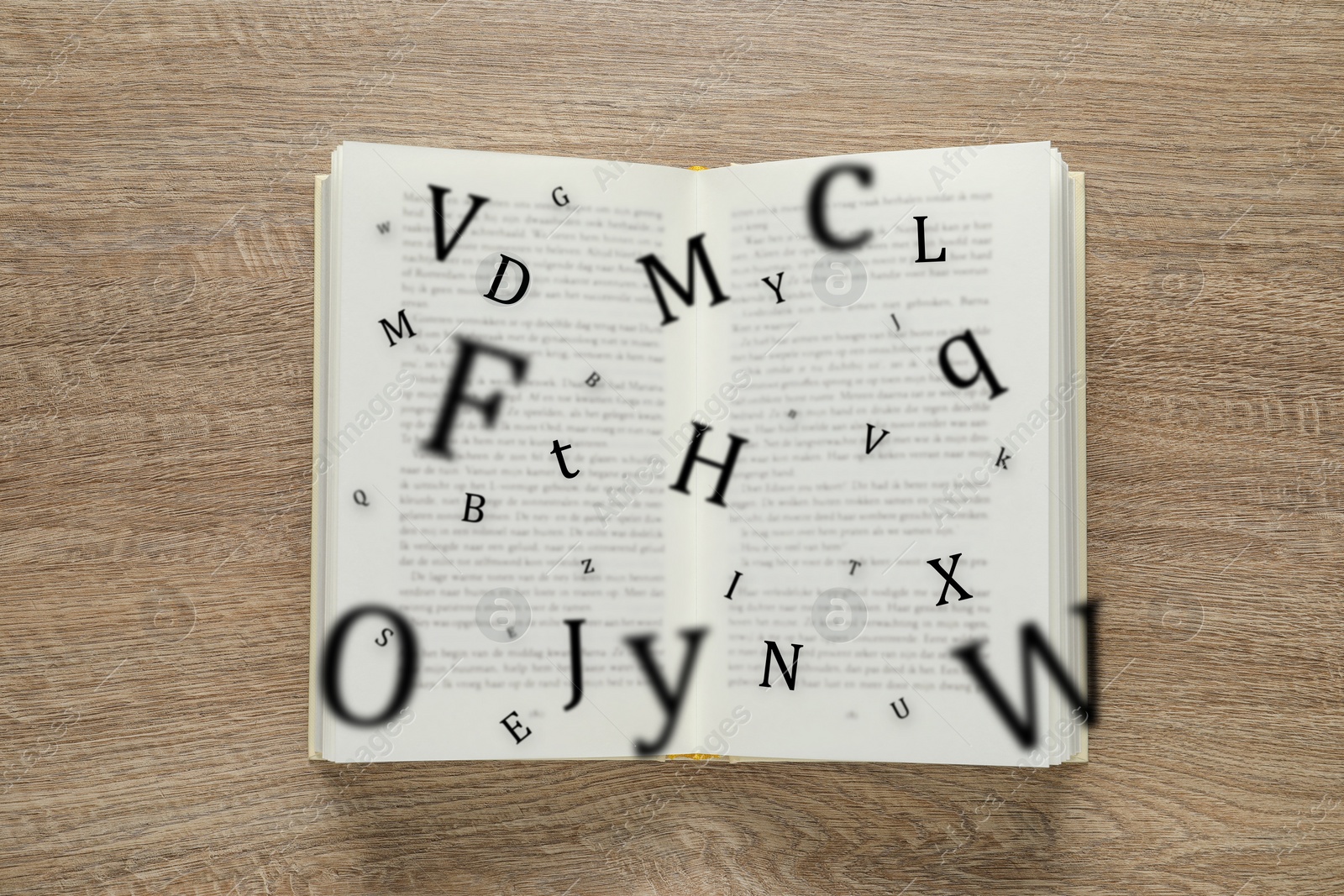 Image of Open book with letters flying out of it on wooden background, top view