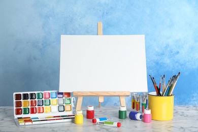 Wooden easel with blank canvas board and painting tools for children on table near color wall