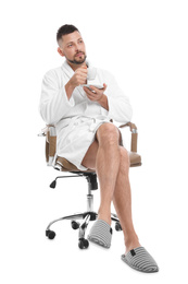 Photo of Handsome man with cup of coffee wearing bathrobe sitting in chair on white background