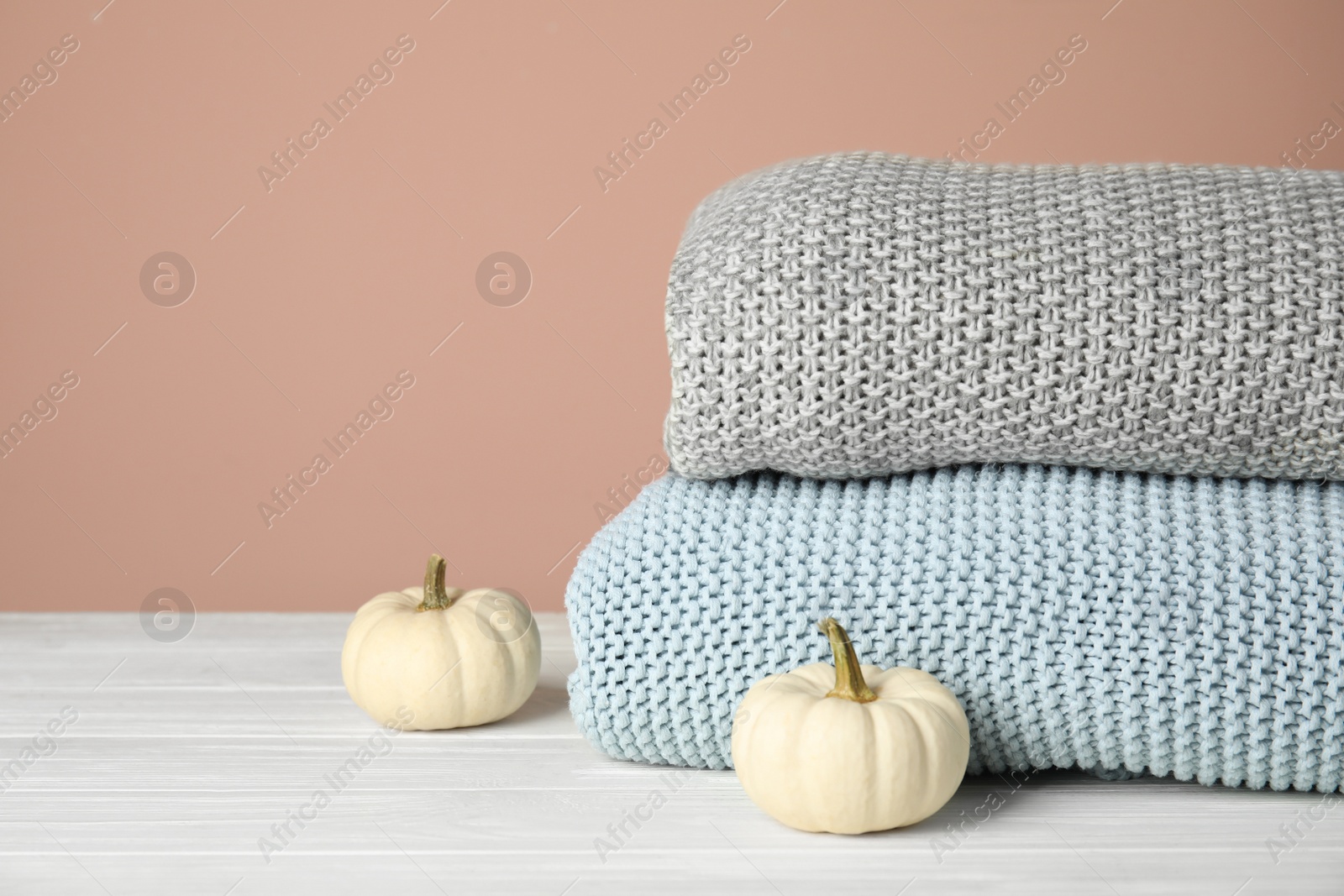 Photo of Soft plaids and small pumpkins on white wooden table, closeup. Space for text