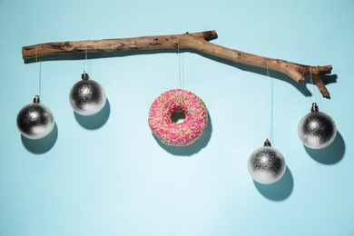 Photo of Silver baubles and donut hanging on tree branch against light blue background