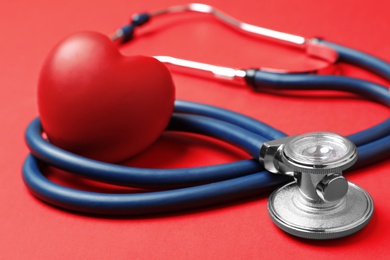 Photo of Red heart with stethoscope on color background, closeup
