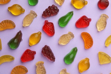 Tasty jelly candies in shape of different fruits on lilac background, flat lay