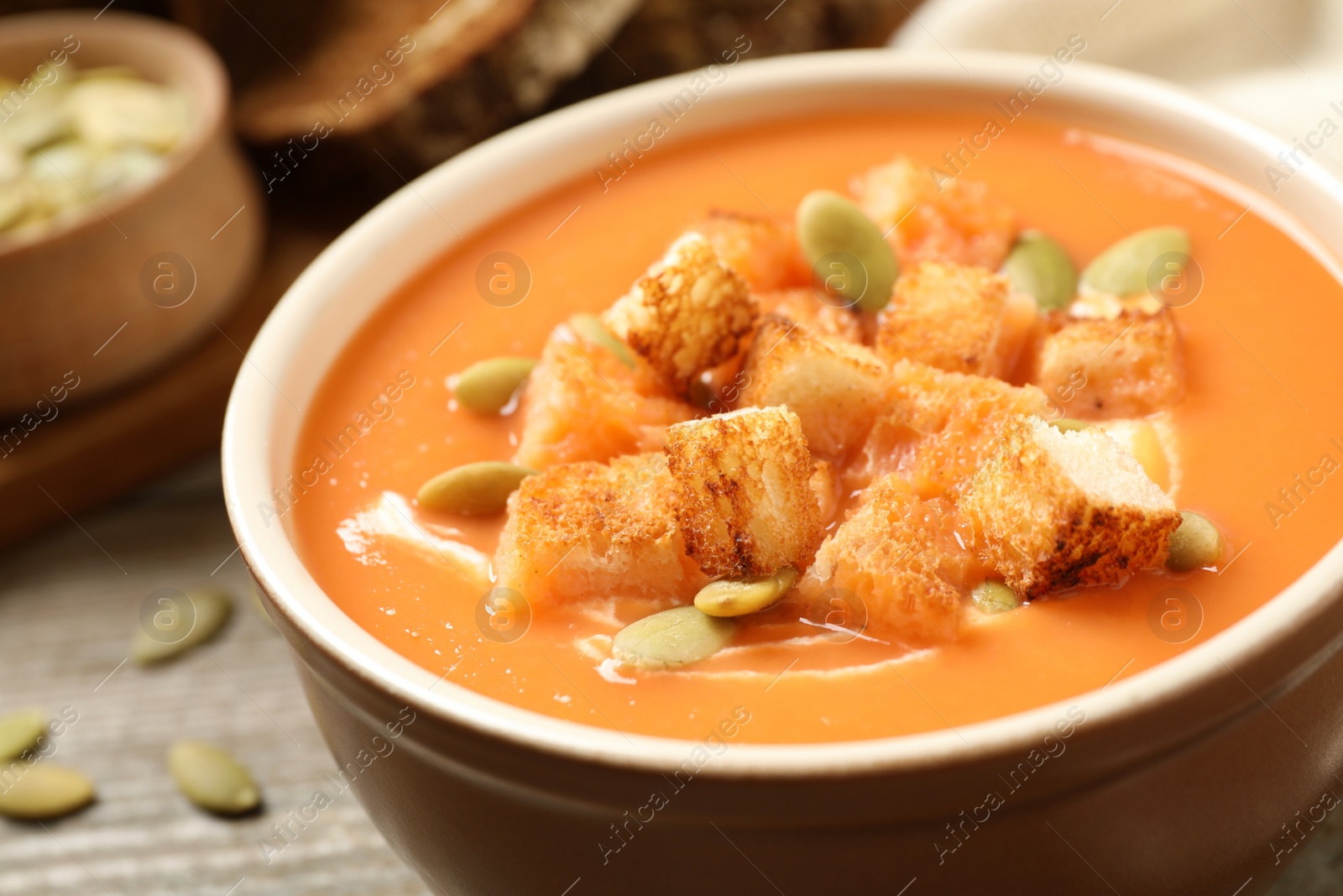 Photo of Tasty creamy pumpkin soup with croutons and seeds in bowl on table, closeup