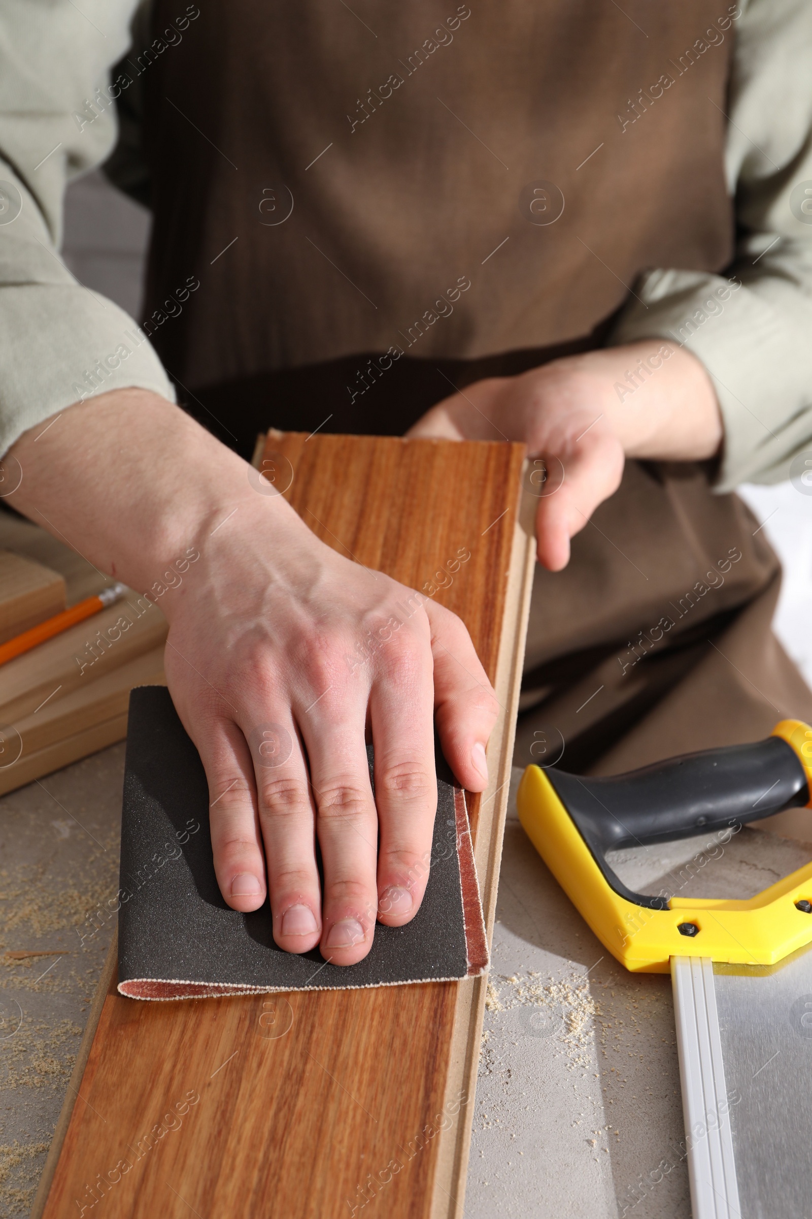 Photo of Man polishing wooden plank with sandpaper at grey table, closeup