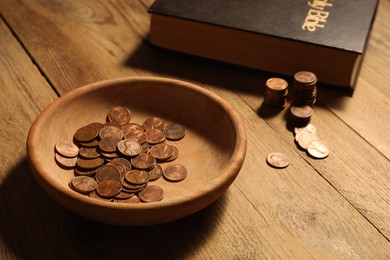 Photo of Donate and give concept. Bowl with coins and Bible on wooden table, closeup