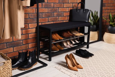 Photo of Stylish hallway with shoe storage bench and accessories near brick wall. Interior design