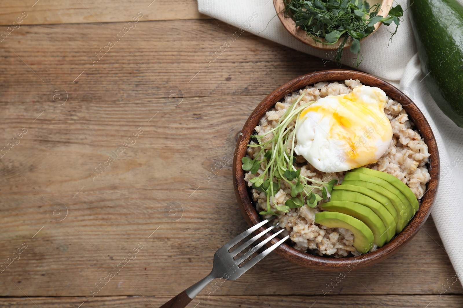 Photo of Delicious boiled oatmeal with poached egg, avocado and fork on wooden table, flat lay. Space for text