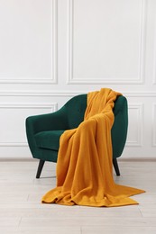 Comfortable armchair with blanket near white wall indoors