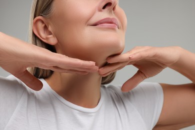 Photo of Mature woman touching her neck on grey background, closeup
