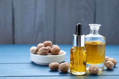 Photo of Bottles of nutmeg oil and nuts on blue wooden table, space for text