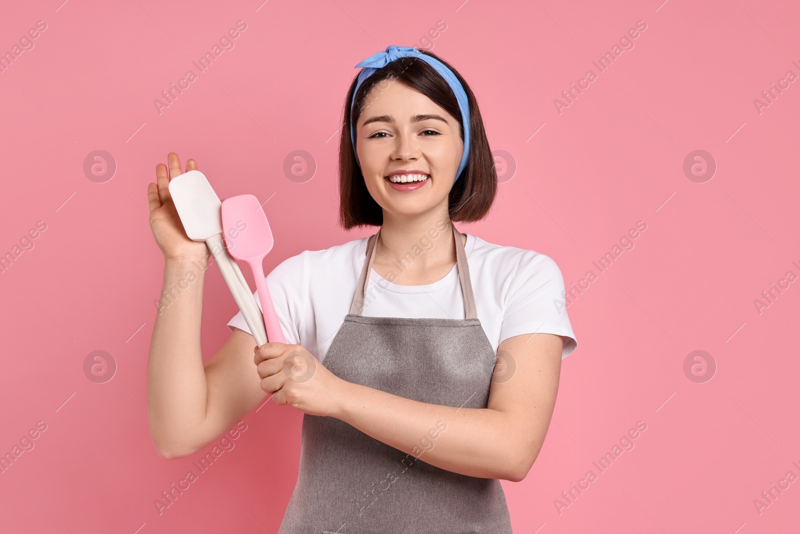 Photo of Happy confectioner with spatulas on pink background