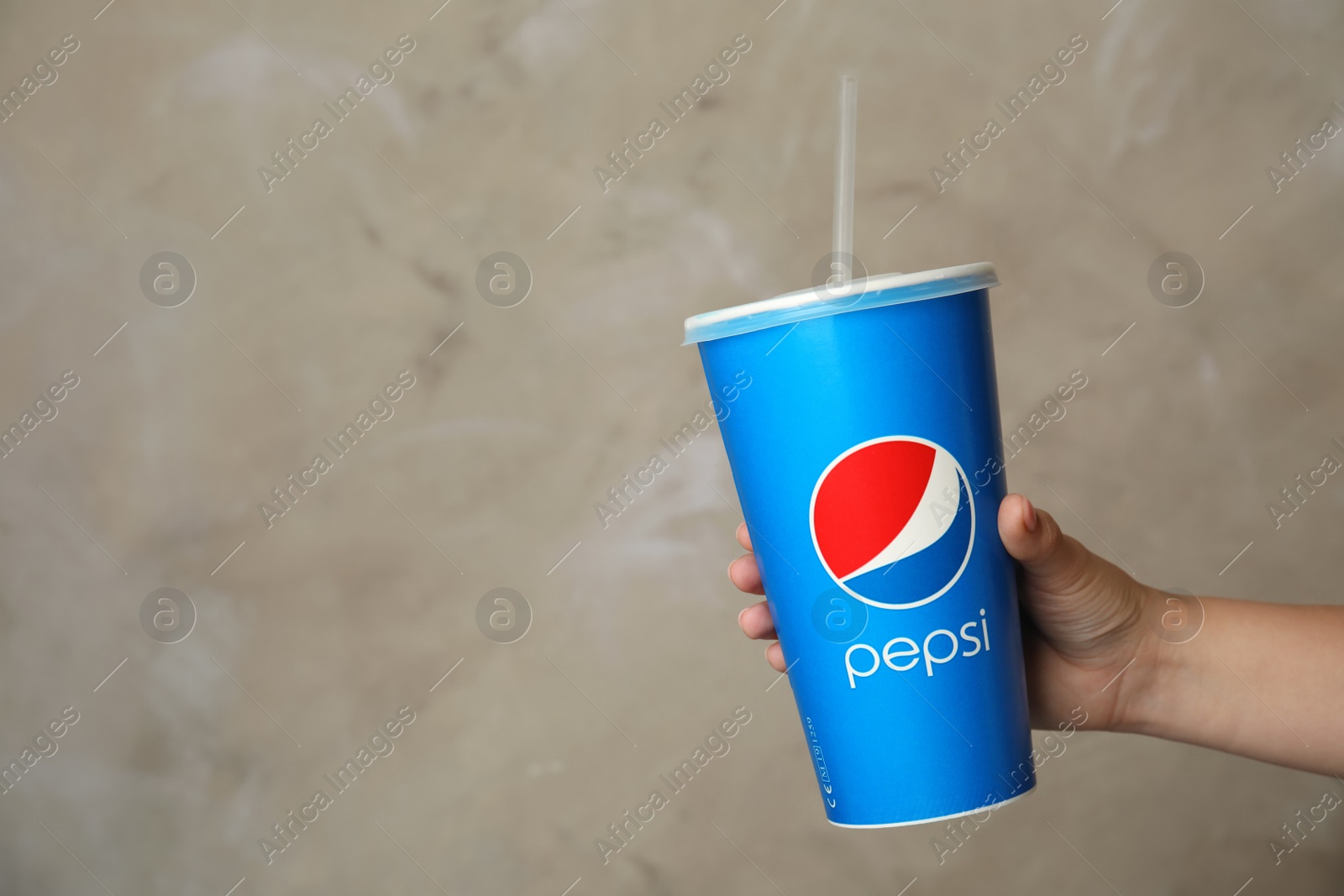 Photo of MYKOLAIV, UKRAINE - JUNE 9, 2021: Woman holding paper Pepsi cup on beige background, closeup. Space for text